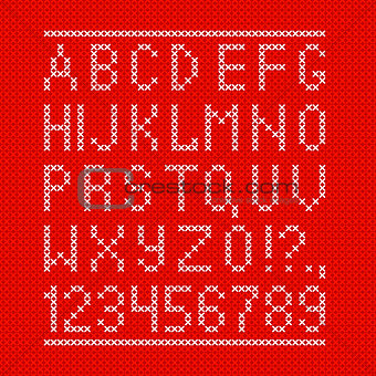 Embroided by cross stitch english alphabet with numbers and symbols on red cloth texture.