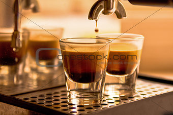 A shot of coffee pouring into two espresso cups