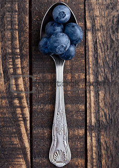 Blueberries on old spoon on grunge wooden board