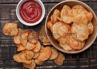 Bowl with potato crisps chips and ketchup on wooden board