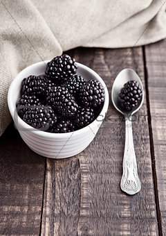 Blackberry in white bowl and spoon on grunge wooden board