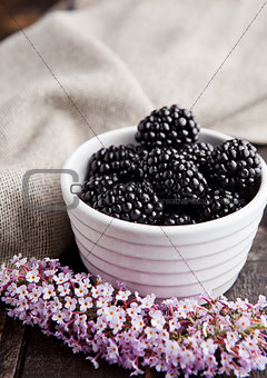 Blackberry in white bowl and flowers on wooden background