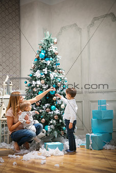 Young woman with two sons decorating on Christmas tree at home