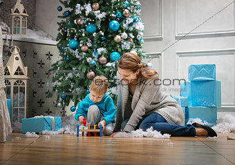 Preschool boy and his mom playing with wooden hammer toy while sitting beside Christmas tree