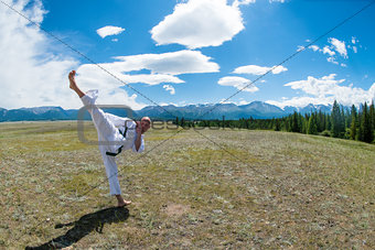 Man in white kimono and black belt training karate on mountain background.