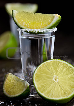 Tequila silver shot with lime slices and salt on wooden board