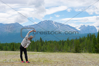 Male runner stretching outdoors at mountains background. Standing quadriceps quad stretch. Walking Heel to Butt.