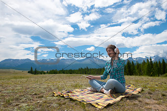 Woman in headphones listening music in a field and at the mountain.