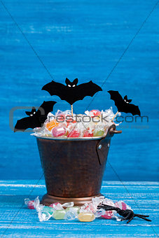 Halloween candy bucket, paper bats and rubber spider on blue woo