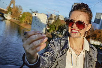 trendy woman with shopping bag taking selfie with phone in Paris