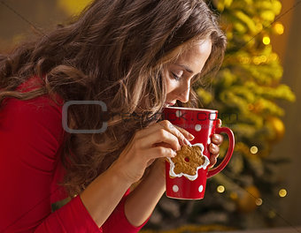 Woman having cup of hot chocolate and cookie near Christmas tree