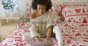 Woman in oversized sweater on bed using laptop
