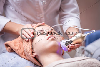 Young woman receiving facial treatment with electroporation beauty device
