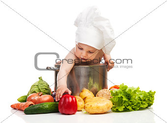 Little boy in chef's hat reaching for bell pepper while sitting in large casserole