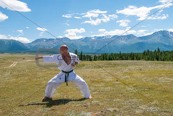 Man in white kimono and black belt training karate on mountain background.