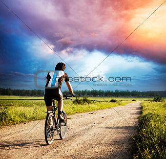 Man Riding a Bike on Country Road at Sunset