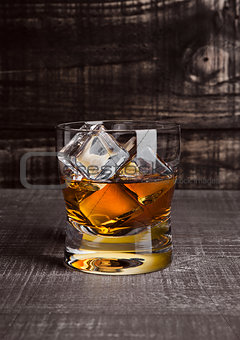 Glasss of whiskey with ice cubes on wood 