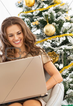 Happy young woman using laptop near christmas tree