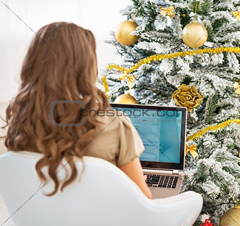 Woman using laptop near christmas tree . rear view