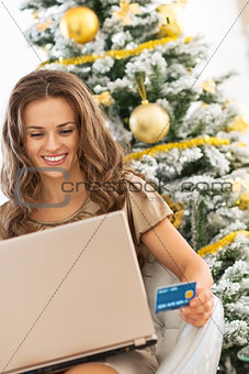 smiling young woman with credit card using laptop near christmas