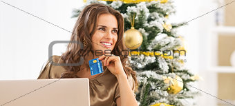 Portrait of thoughtful young woman with credit card using laptop