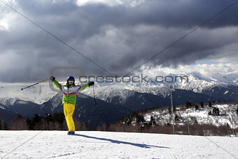 Happy young skier with ski poles in sun mountains and cloudy gra