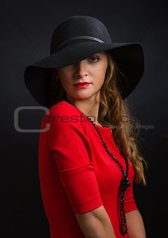 The beautiful young girl in a bright red dress and  black hat with the wide fields
