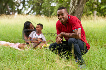 Confident Black Man Smiling At Camera And Family Doing Picnic
