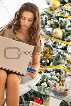 Young woman making online shopping while sitting near christmas 