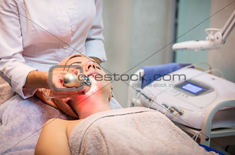 Young woman receiving facial treatment with electroporation beauty device