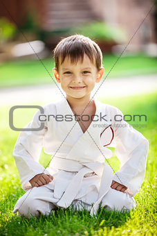 Smiling little boy in kimono sitting on grass in park