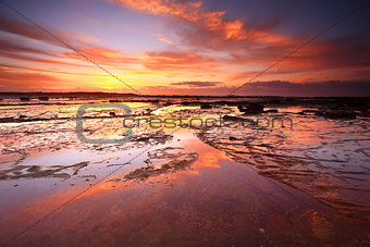 Sunrise skies reflecting on the exposed rocks in low tide