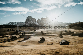 Wooden houses on a field at the foot of a mountain range.
