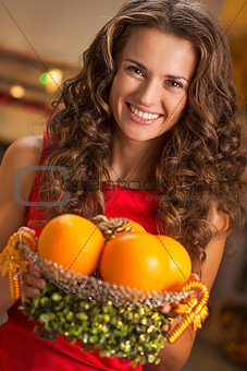 Portrait of happy young housewife showing plate of oranges