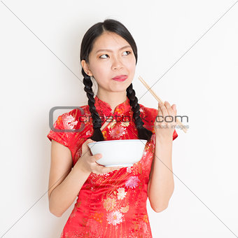 Oriental girl in red qipao eating with chopsticks
