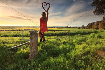 Escape to the Country - female on fence with love heart in morni