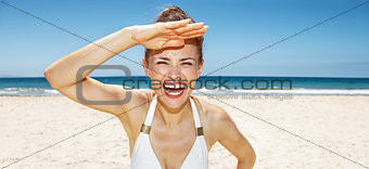 Cheerful woman in white swimsuit at sandy beach on sunny day