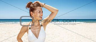Happy woman in white swimsuit at sandy beach looking aside