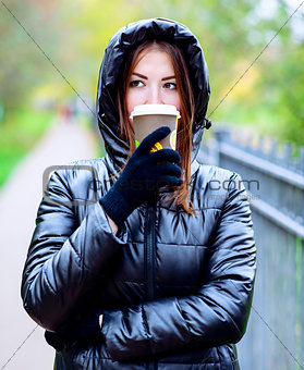 Girl in jacket with hood, holding a coffee or tea, young enjoys the outdoors and sports, spring  autumn, lifestyle, black , the concept of breakfast, gloves