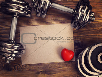 metal dumbbells and red heart on a wooden background