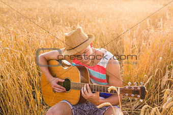 Happy handsome man is playing guitar in the field