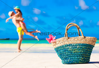 colourful straw beach bag abd hugging honeymoon couple on background
