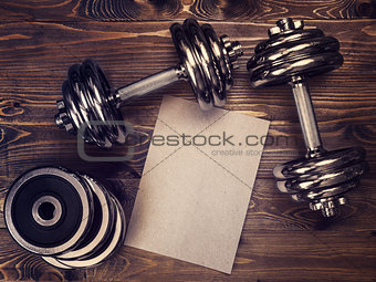 Toned image of metal dumbbells and a sheet of craft paper