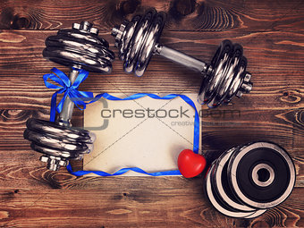 Toned image of metal dumbbells, blue atlas ribbon, red heart and a sheet of craft paper