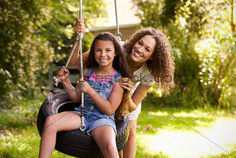 Mother Pushing Daughter On Tire Swing In Garden