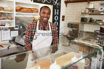 Man behind the counter at a sandwich bar looking to camera