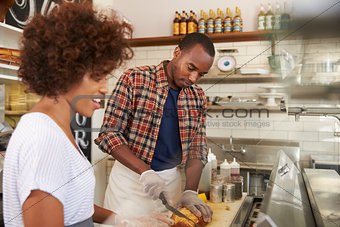 Black couple prepare food behind counter at a sandwich bar