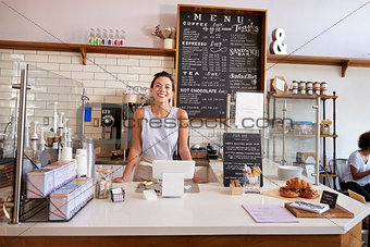 Woman behind the counter of a coffee shop looking to camera
