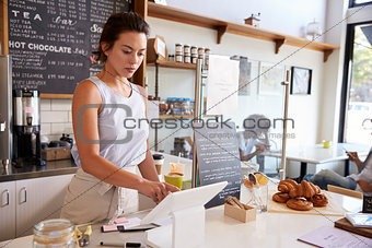 Woman working on the till at a coffee shop, wide angle