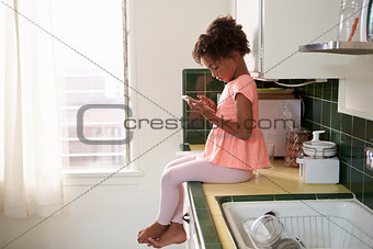 Young Girl Sits In Kitchen And Plays With Mobile Phone